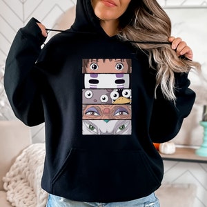 Op de afbeelding: Zwart hoodie met een grafische print van personages uit de animatiefilm Spirited Away. De grafiek toont close-ups van de ogen van Chihiro, No-Face, de badhuisgeesten, Yubaba en de witte wolf.