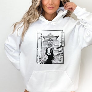 Op de afbeelding: Witte hoodie met een zwart-witte grafische print van een personage uit de film Spirited Away. De afbeelding bevat de Japanse tekst "千と千尋の神隠し", wat "Spirited Away" betekent.