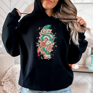 Op de afbeelding: Zwarte hoodie met een kleurrijke illustratie van een draak met een speer. De draak is wit, groen en oranje, met Japanse tekst eronder. Het ontwerp staat tegen een bruin en rood gespikkeld achtergrond.
