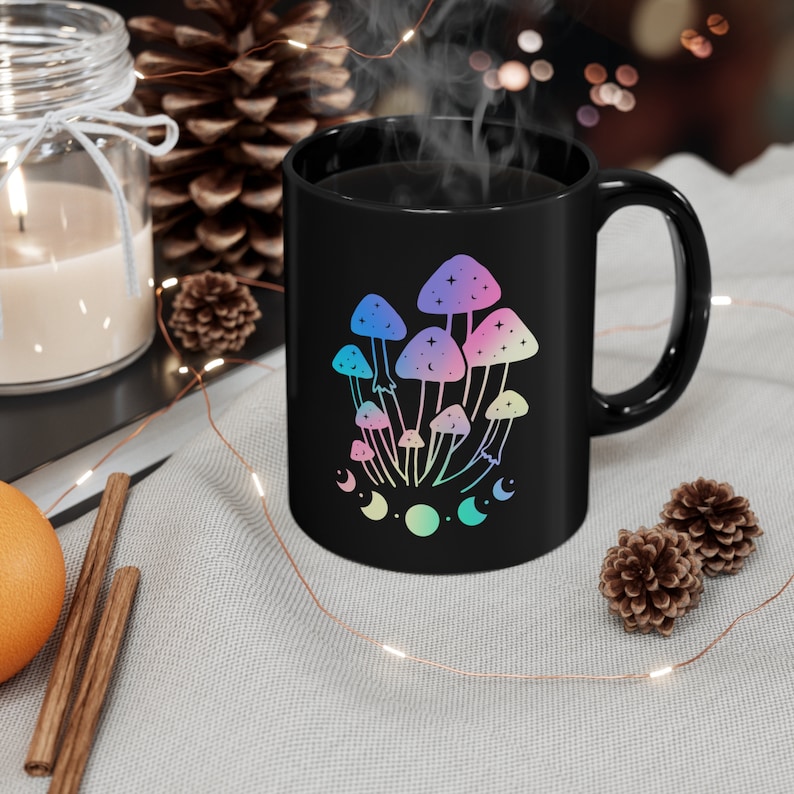 Puede incluir: Taza de cer&aacute;mica negra con un dise&ntilde;o de setas de colores arco&iacute;ris y un patr&oacute;n de luna creciente. La taza est&aacute; llena de un l&iacute;quido oscuro y sale vapor de ella.