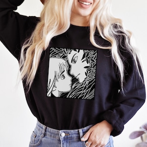Op de afbeelding: Zwart sweatshirt met een witte grafische print van twee anime-personages die elkaar aankijken. De personages zijn omringd door zwart en wit gebladerte.