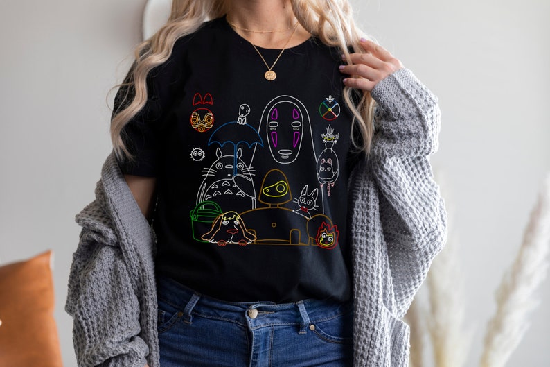 May include: Black t-shirt with a colorful outline design of characters from the Studio Ghibli film, Spirited Away. The characters include No Face, Totoro, Jiji, and others.