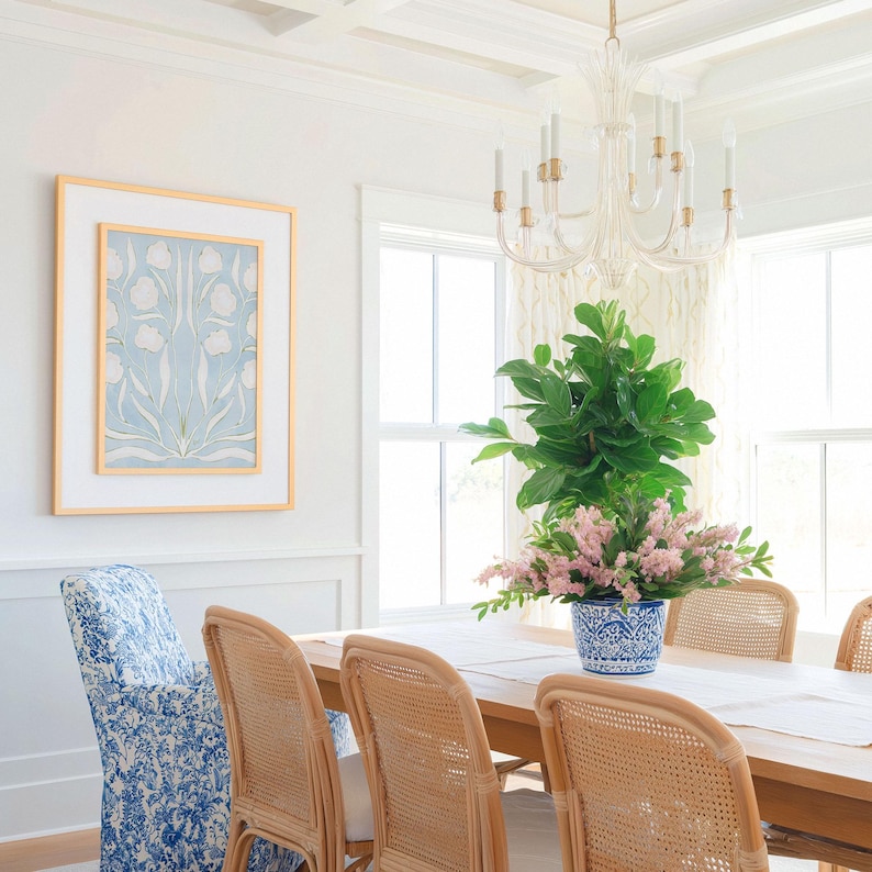 a dining room with a wooden table and chairs, a chandelier hanging above, and a large potted plant on the table. The room has white walls and a blue and white floral patterned chair.