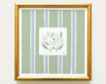 May include: A square framed print featuring a central white panel with a hand-painted illustration of four light blue flowers and green leaves. The background consists of vertical sage green and light blue stripes. The frame is metallic gold.