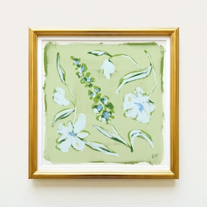 The image is a framed painting of white flowers with green leaves, displayed on a white wall.