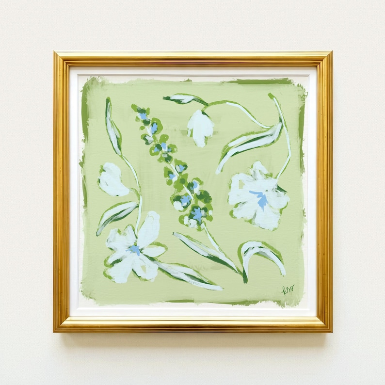 The image is a framed painting of white flowers with green leaves, displayed on a white wall.