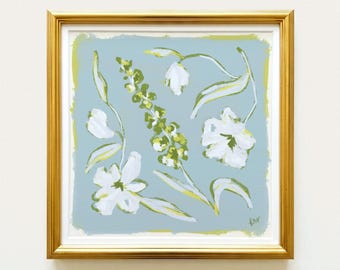 May include: A square framed painting featuring white flowers and green foliage on a light blue background. The artwork is enclosed in a metallic gold frame with a white mat border. The painting displays loose brushstrokes and a signature in the corner.