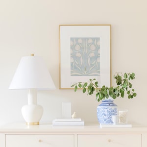 a white dresser with a lamp, a framed picture, a blue and white vase with greenery, and some books and a small bird figurine on top.