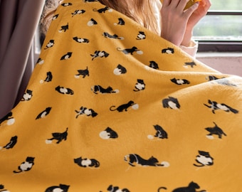 May include: A yellow blanket with a black cat pattern. A person is sitting on the blanket and holding a yellow mug.