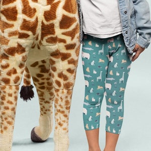 Puede incluir: Una gran jirafa de peluche con un patrón de manchas marrones y crema. La jirafa está de pie junto a una niña que lleva una camiseta blanca, una chaqueta vaquera y leggings estampados. La jirafa mide aproximadamente 183 cm de altura.