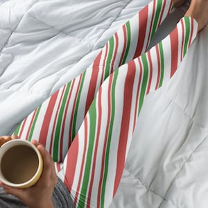 Może przedstawiać: Czerwono-biało-zielone, pasiasty leggings. Leggings są noszone przez osobę siedzącą na białym łóżku.