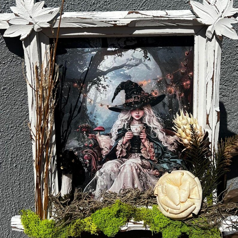 May include: A framed artwork featuring a fantasy scene of a witch in a forest, holding a teacup. The artwork is in a distressed white wooden frame, decorated with dried plants and moss. The witch wears a black hat and gown.