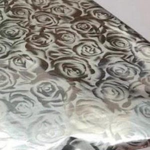 May include: A sheet of metallic silver wrapping paper featuring a repeating pattern of dark gray roses. The surface has a highly reflective, mirror-like finish that creates a contrast between the light silver background and the darker floral shapes.