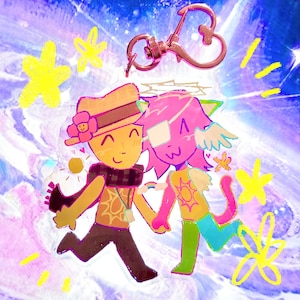 May include: A whimsical keychain featuring a cartoon illustration of two figures holding hands, set against a vibrant, swirling background with star accents. The figures are in shades of orange, pink, and green, with a heart-shaped clasp at the top.