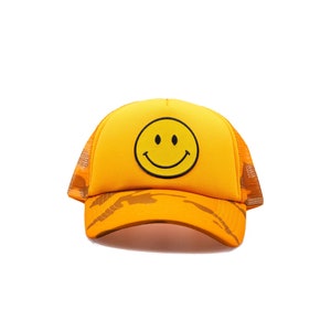 May include: A yellow and brown camouflage trucker hat with a yellow smiley face embroidered on the front.