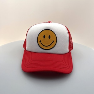 May include: A red and white trucker hat with a yellow smiley face embroidered on the front.