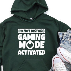 May include: A dark green hooded sweatshirt with the text "Do Not Disturb Gaming Mode Activated" in white. The text is in a box with a power button symbol.