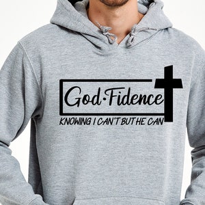 Może przedstawiać: Szara bluza z kapturem z czarnym nadrukiem, na kt&oacute;rym widnieje napis "God-Fidence" z krzyżem i tekstem "Knowing I can't but He can".