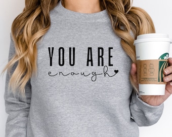 May include: Gray sweatshirt with the text "YOU ARE enough" in black lettering with a small heart symbol.