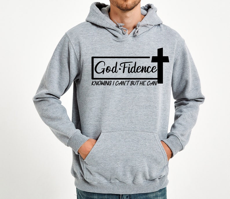 Może przedstawiać: Szara bluza z kapturem z czarnym nadrukiem, na kt&oacute;rym widnieje napis "God-Fidence" z krzyżem i tekstem "Knowing I can't but He can".