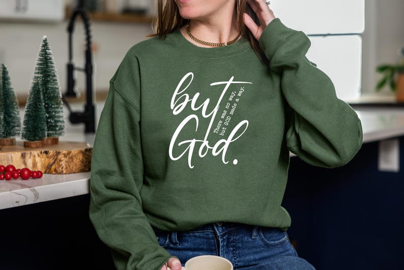 May include: A dark green sweatshirt with the words "but God" in white script. The text "There was no way, but GOD made a way" is also printed on the shirt. The person is wearing blue jeans.