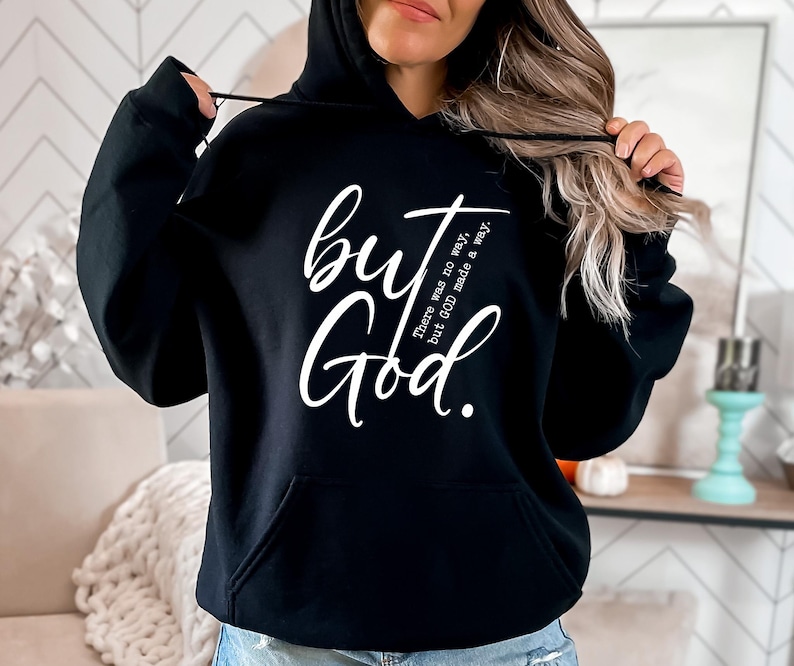 May include: Black hooded sweatshirt with the words "but God" in a white script font. The phrase "There was no way, but GOD made a way" is printed in a smaller font. The sweatshirt has a front pocket and a drawstring hood.
