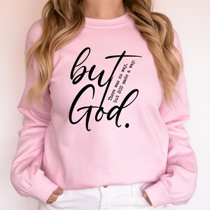 May include: A light pink sweatshirt with long sleeves. The front of the sweatshirt features the words "but God" in a large, black, cursive font. Below the word "but" is the text "There was no way, but GOD made a way."