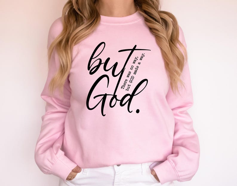 May include: A light pink sweatshirt with long sleeves. The front of the sweatshirt features the words "but God" in a large, black, cursive font. Below the word "but" is the text "There was no way, but GOD made a way."