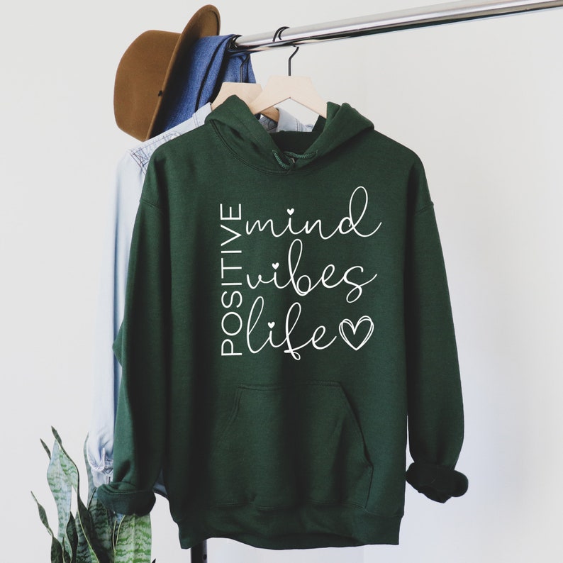 May include: A dark green hooded sweatshirt with the text "POSITIVE mind vibes life" in white lettering with small hearts.