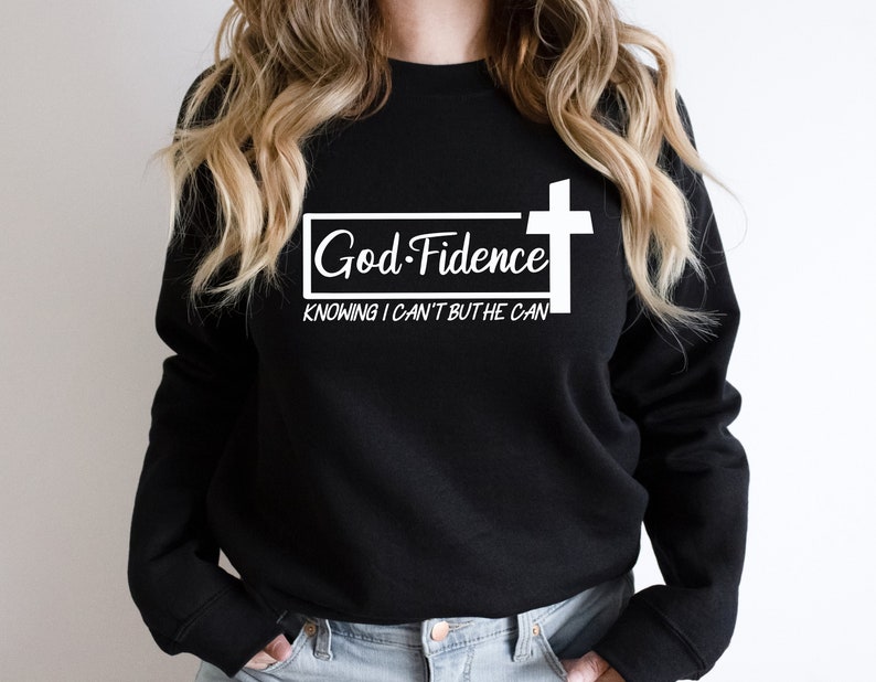 Może przedstawiać: Czarna bluza z białym napisem "God-Fidence" i "Knowing I can't but He can" oraz białym graficznym krzyżem.