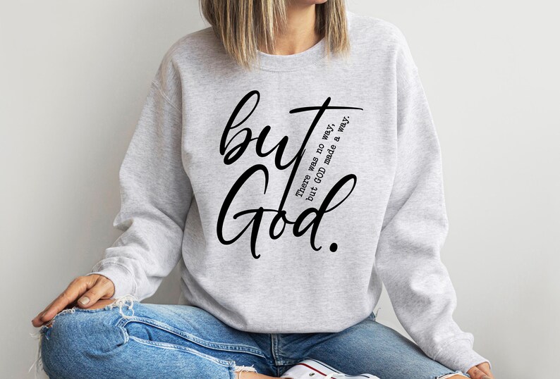 May include: A light gray sweatshirt with the words "but God" in large, black script. The phrase "There was no way, but GOD made a way" is printed in smaller, black text. The sweatshirt is a casual style.