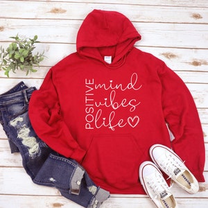 May include: Red hooded sweatshirt with the text "POSITIVE mind vibes life" in white lettering with a small heart at the end.