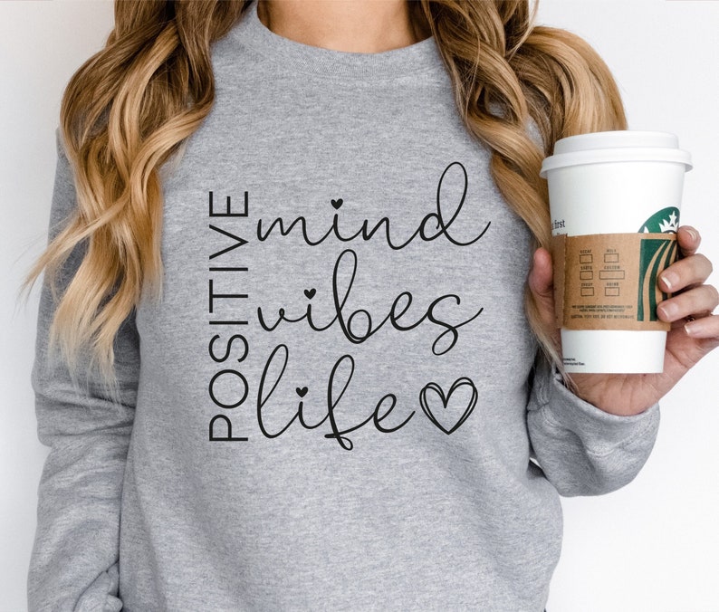 May include: A gray sweatshirt with the text "POSITIVE mind vibes life" in black script with small hearts. The text is centered on the front of the sweatshirt.