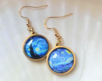 May include: A pair of gold-colored dangle earrings. Each earring features a round, gold-toned frame with a glass-covered image of Van Gogh's "Starry Night" painting in shades of blue, yellow, and black. The earrings hang from gold-colored fish hook ear wires.