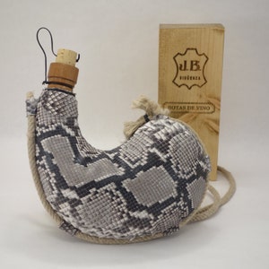 May include: A gray and black snakeskin wine bottle with a cork stopper and a rope handle. The bottle is in a wooden box with the text "J.B.  BIGORRENZA  BOTAS DE VINO" on the front.