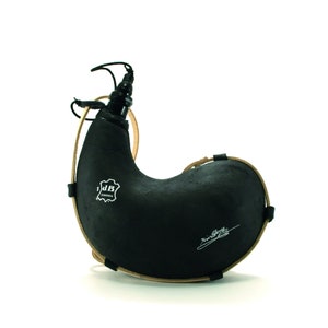 May include: A black leather flask with a brown leather strap and a metal spout. The flask has a label that says "J.B. Barcelona" and a signature on the side.