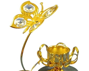 May include: Gold metal candle holder with a butterfly design. The butterfly has clear crystal accents. The candle holder has a round base and a cup for a candle.