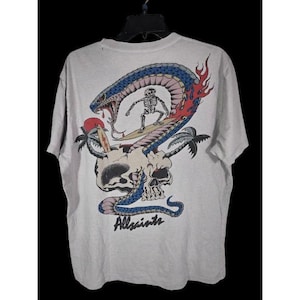 May include: A light gray t-shirt featuring a colorful graphic. The design includes a skull, a snake, a skeleton surfing, palm trees, and flames. The word "Allsaints" is printed at the bottom of the design.