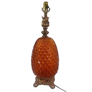 May include: A vintage table lamp with a pineapple-shaped amber glass shade. The lamp has a brass-colored base and accents, and a standard light bulb socket. The lamp is approximately 20 inches tall.