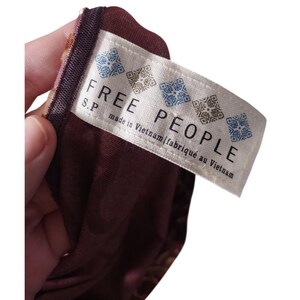 May include: A close-up of a burgundy fabric with a tag that reads "FREE PEOPLE" in large, bold letters. The tag also includes the text "made in Vietnam | fabriqu&eacute; au Vietnam". The fabric has a floral pattern.
