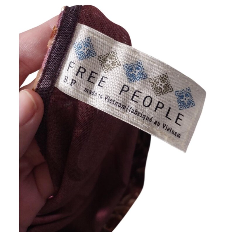 May include: A close-up of a burgundy fabric with a tag that reads "FREE PEOPLE" in large, bold letters. The tag also includes the text "made in Vietnam | fabriqu&eacute; au Vietnam". The fabric has a floral pattern.