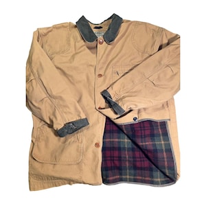May include: A tan canvas field jacket featuring a dark green corduroy collar and matching sleeve cuffs. The jacket has a button-front closure, two large front patch pockets, and a visible interior lining with a red, green, and yellow plaid pattern.