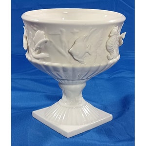 May include: White ceramic bowl with a pedestal base. The bowl is decorated with raised sea life designs, including fish, seahorses, and seaweed.
