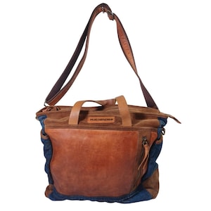 May include: A brown leather and suede shoulder bag with a denim accent. The bag has a top handle and a long adjustable strap. The front features a large leather pocket and a zipper pocket. The word "TASCHENDEE" is embossed on the top.