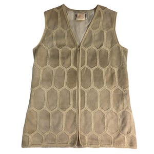 May include: A beige sleeveless vest featuring a repeating hexagonal pattern constructed from stitched panels. The garment has a central front zipper closure and a V-neckline, with a visible interior label at the neck. The surface has a matte texture.
