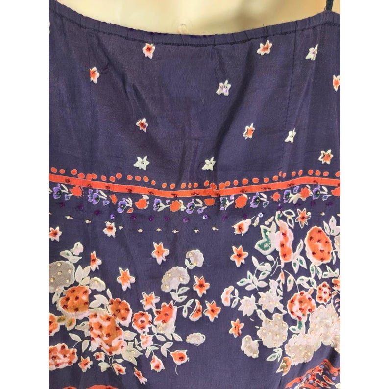 Puede incluir: Vestido de verano azul oscuro con estampado floral. El vestido presenta flores naranjas, blancas y grises, con detalles en naranja y morado. La parte superior del vestido tiene peque&ntilde;os dise&ntilde;os blancos en forma de estrella.