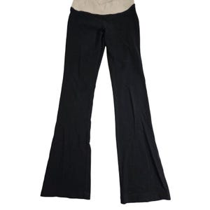 May include: Black maternity pants with a beige waistband. The pants have a flared leg design and are made of a soft, stretchy material. These pants are designed for comfort and support during pregnancy.