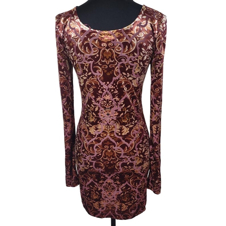 May include: A burgundy long-sleeve dress with an ornate, floral pattern in shades of gold and pink. The dress has a scoop neckline and a fitted silhouette, suitable for various occasions.