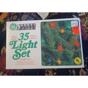 May include: A box of GE Merry Midget 35 Light Set for indoor or outdoor use. The box features a picture of a lit Christmas tree. The text on the box reads "Straight Line" and includes information about the light set.