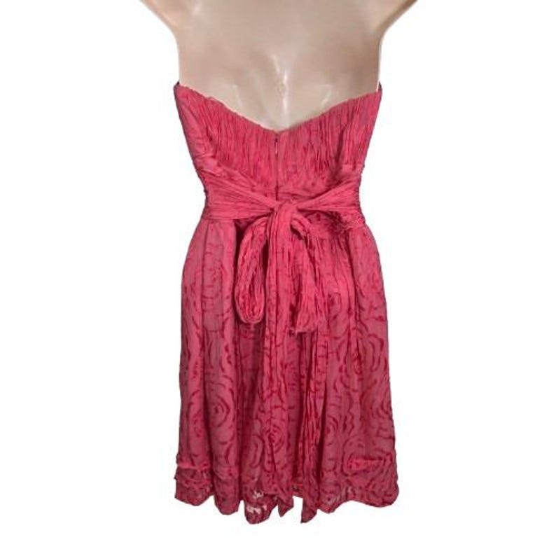 May include: A strapless, knee-length pink dress. The dress features a textured bodice and a bow at the waist. The skirt has a subtle floral pattern. The dress is displayed on a mannequin.